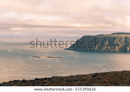 Rocky coast with big cliffs falling into a calm sea at sunset with pink clouds in the sky