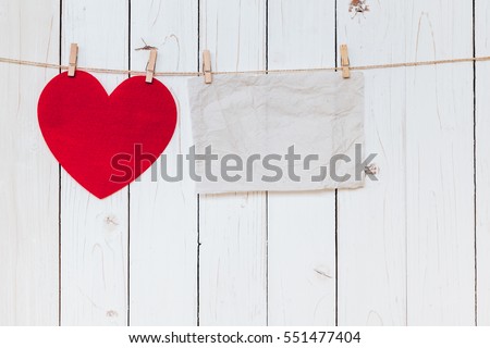 Red heart and old paper blank hanging at clothesline on wood white background with space. Valentine Day.