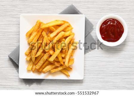 Fresh homemade crispy French fries on plate with a small bowl of ketchup on the side, photographed overhead with natural light   Royalty-Free Stock Photo #551532967