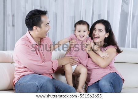 Picture of an Asian young father and his wife embracing their child while sitting on the couch
