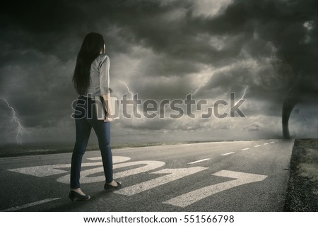 Picture of a female employee walking on the road while carrying a laptop with storm on the sky