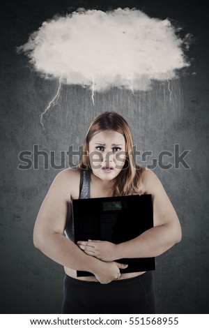 Depressed woman with overweight body holding a weighing scale under speech bubble