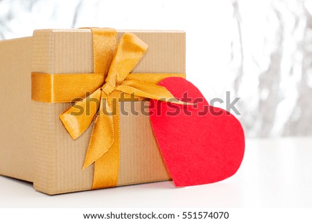 gift box with Golden ribbon and red heart lies on a white table on silver glittering background. festive concept for Valentine's day, birthday, wedding, party, holiday