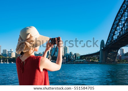 Woman in red top and summer hat taking pictures of Sydney Harbour Bridge with view of Milsons point on the background Royalty-Free Stock Photo #551584705