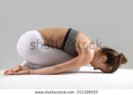 Young attractive woman practicing yoga, sitting in Child exercise, Balasana pose, working out wearing sportswear, white pants, bra, indoor full length, isolated against grey studio background Royalty-Free Stock Photo #551588929