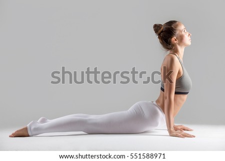 Young attractive woman practicing yoga, stretching in Cobra exercise, Bhujangasana pose, working out wearing sportswear, indoor full length, isolated against grey studio background Royalty-Free Stock Photo #551588971