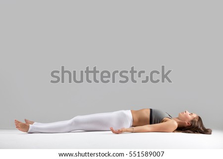 Young attractive woman practicing yoga, lying in Dead Body, Corpse exercise, Savasana pose, working out wearing sportswear, indoor full length, isolated against grey studio background Royalty-Free Stock Photo #551589007