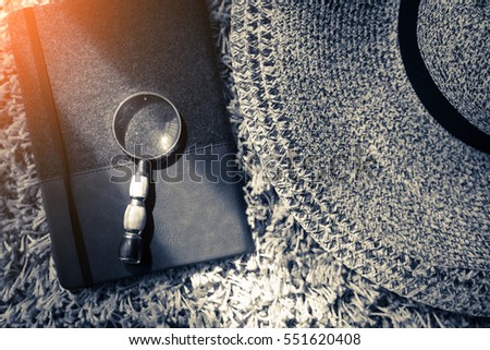 travel concept stuff with woman hat notebook magnifying glass on carpet in bedroom with light glow from window curtain daytime