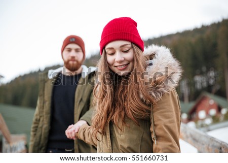 Picture of young cheerful loving couple walking over mountains and looking aside.
