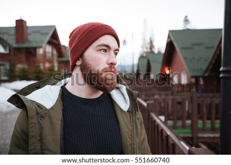 Picture of young handsome bearded man standing outdoors and looking aside.