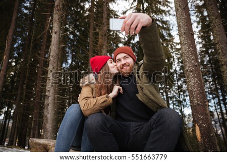 Picture of young happy loving couple sitting over forest and hugging while make selfie.