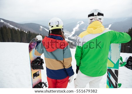 Back view photo of young loving couple snowboarders on the slopes frosty winter day.