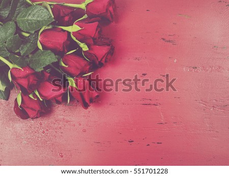 Happy Valentines Day background with red roses on distressed vintage recycled wood table with applied faded retro style filters.