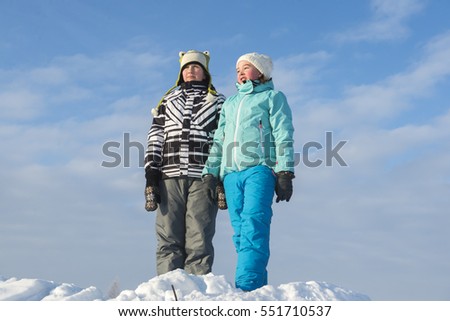 Two teenage girls in winter clothes standing in snow against blue sky