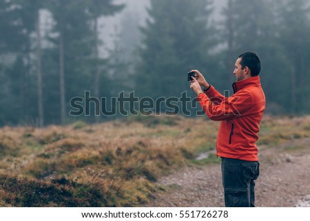 Young man taking a picture with a smart phone in a foggy and rainy weather