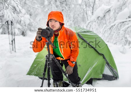 Young professional caucasian photographer with photo camera on tripod in the snowy winter forest
