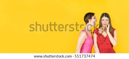 Two women whispering gossip or bad news. Isolated studio yellow background female model. Banner edition.