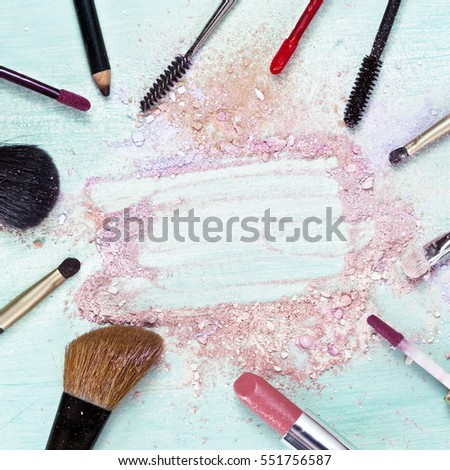 Makeup brushes and lipstick on teal blue background, with traces of powder and blush, forming a frame; square template for makeup artist's business card or flyer design; with copyspace