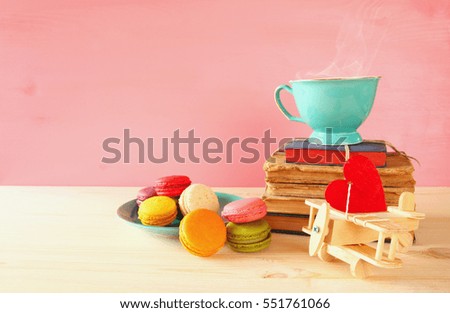 Mint vintage cup of coffee and colorful macaron or macaroon next to stack of books on wooden table over pink background