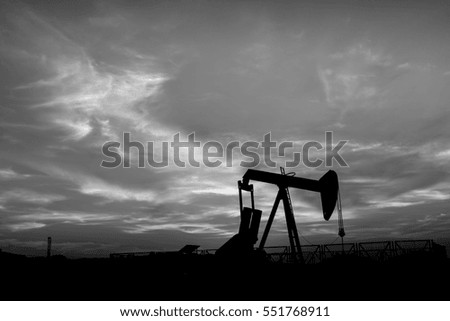 Silhouette of crude oil pump at sunset blue hour in the oilfield - black and white 
