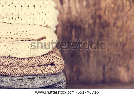 A stack of woolen sweater, plaid. Warm clothing. Home atmosphere, winter clothing. Gray, white and brown sweater. Warm and cozy. Knitted clothes. Cozy atmosphere.