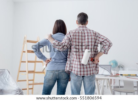Loving couple staring at their freshly painted room, back view: home renovation and relationships concept Royalty-Free Stock Photo #551806594
