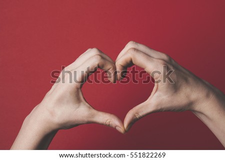 Female hands creating the shape of a love heart over a red background. Romance and valentines day concept