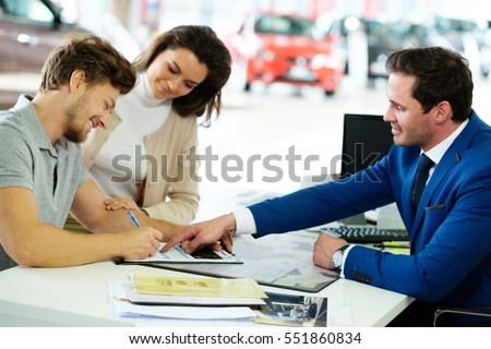 Beautiful young couple signs documents at dealership showroom.