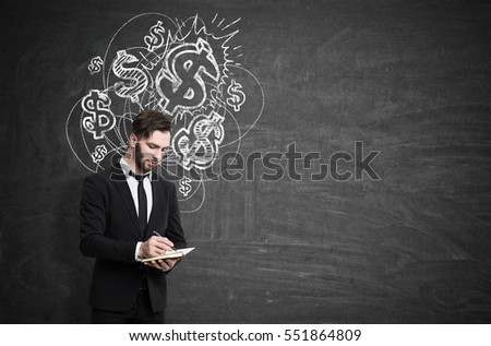 Bearded businessman in a suit is standing near a blackboard with multiple dollar marks sketch and writing in his notebook. Mock up