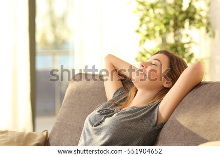 Portrait of a girl relaxing on a sofa after work at home sitting on a sofa in the living room at home with a warm light of sunset Royalty-Free Stock Photo #551904652