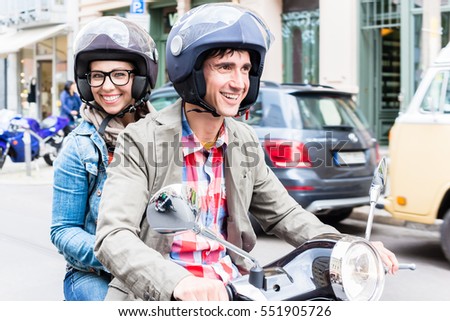 Young woman with helmet sitting on pillion seat of Vespa in streets of Berlin Royalty-Free Stock Photo #551905726