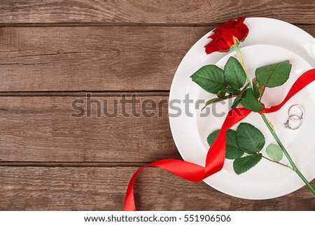 Top view closeup of romantic dinner serving with a red rose and ring above the white plate