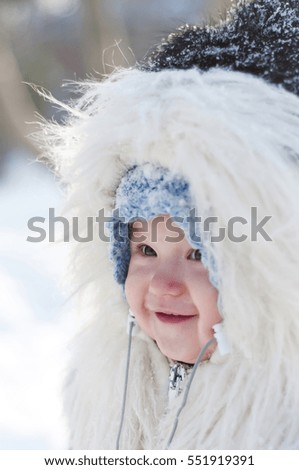 
A cute little girl in a fur coat with a hood in the snow. Snowfall