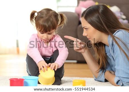 Portrait of a mother scolding to her baby daughter sitting on the floor in the living room at home Royalty-Free Stock Photo #551944534