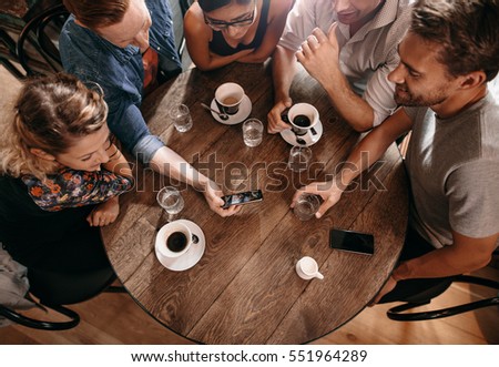 Group of friends at the cafe and looking at smart phone. Man showing something to his friends sitting by.