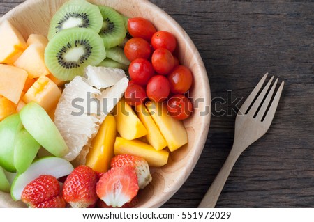 kitchen table with Variety of Fruits on wood plate and fork, group of Fruits salad - healthy eating and dieting food, concept of health care,  Image focus top view.
