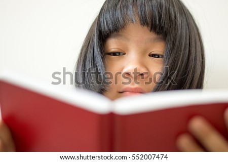 Asia kid girl reading red book at home. Female cute child concentrate on read young adult novel. Asian students study textbook for test. World book day and education concept.