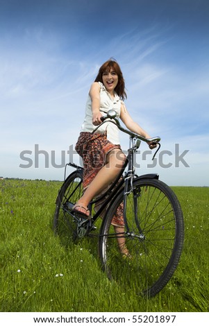 Happy young woman on a green meadow with a vintage bicycle