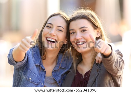 Front view portrait of two funny friends with thumbs up and looking to the camera in the street Royalty-Free Stock Photo #552041890