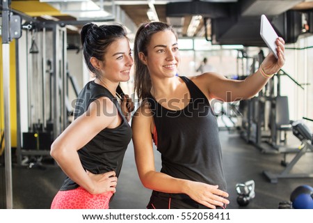 Two female friends taking a selfie photo after hard workout in gym.