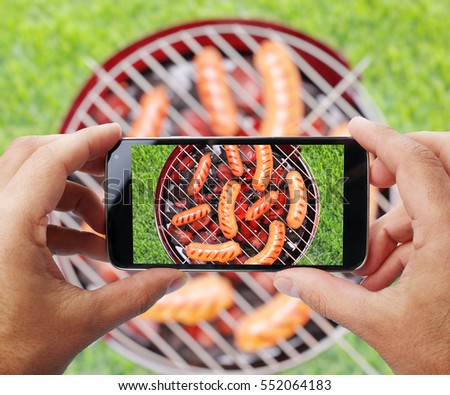 Taking photo of grilling sausages by smartphone. Closeup view of  process. File contains clipping paths for smartphone and it's picture.