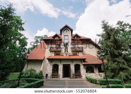 Look from outside at three-storeyed country house surrounded with green trees