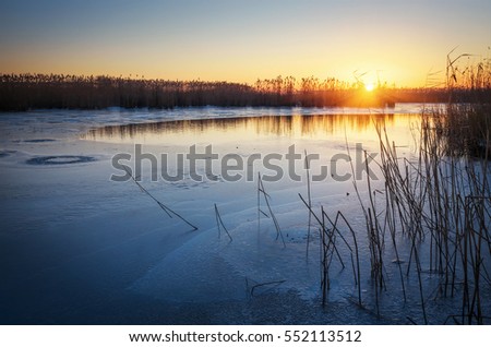Winter landscape with frozen river, reeds and sunset sky. Daybreak
