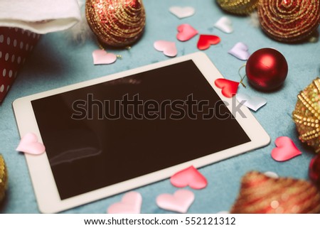 Blurry defocused joyful Christmas decorations, Santa Claus hat and mobile tablet smart computer for photo and video, multimedia presentation
