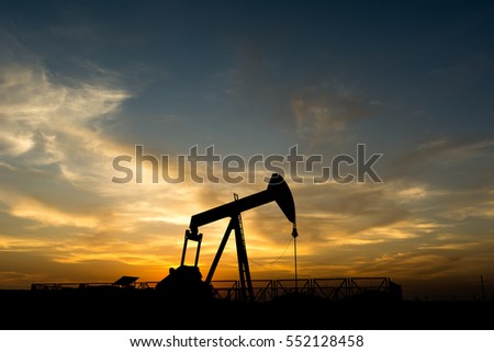 Silhouette of crude oil pump at sunset golden hour in the oilfield
