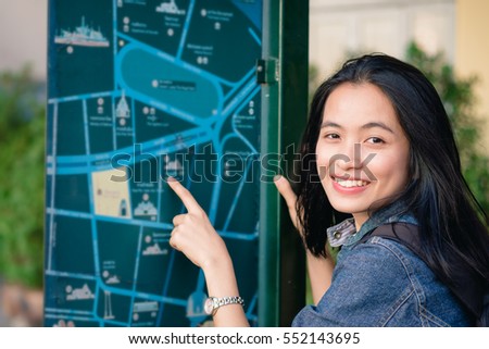 girl smiling on street in Bangkok, point to a map sign on a side walk
