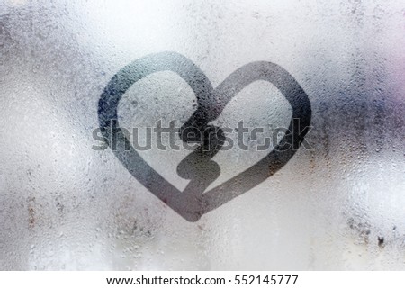 heart broken shape written on a foggy window and rain drops.