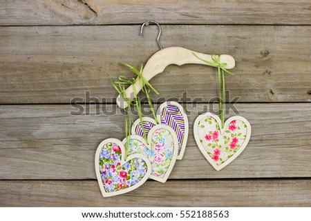 Colorful country fabric hearts hanging by ribbon on clothes hanger with antique rustic wooden background; Valentine's Day, Mother's Day and love concept with wood copy space