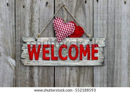 Red welcome sign hanging by rope on antique rustic wood door with red and white gingham heart and red fabric heart; Valentine's Day, love, home and family concept background