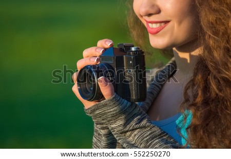 Beautiful girl-photographer with curly hair holding an old camera and take a picture, in the spring outdoors in the park. The concept of tourism and travel.